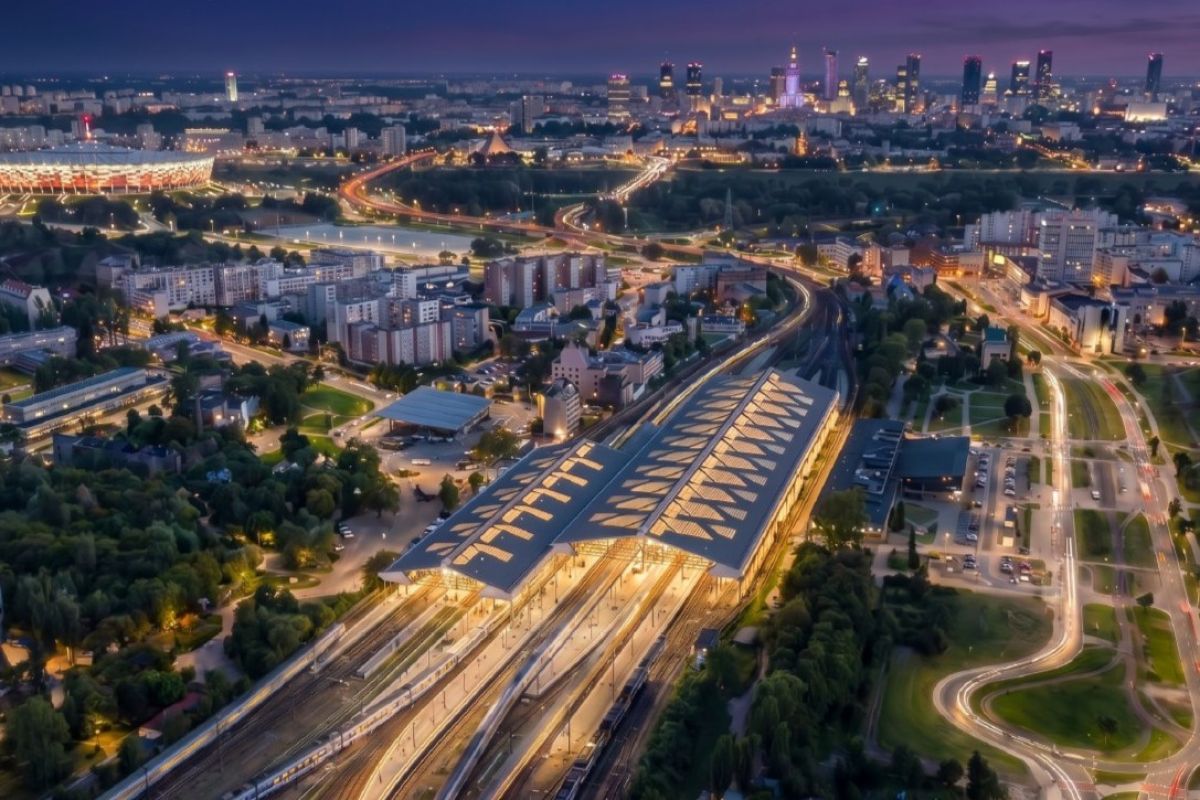 Warszawa Wschodnia railway station at night with illuminated platforms, multiple railway tracks, and surrounding urban infrastructure